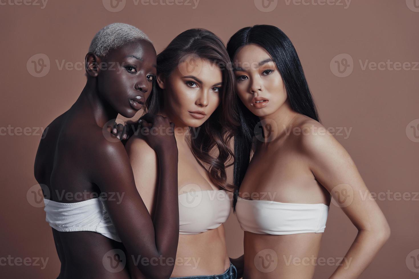 Feeling free and confident. Three attractive young women looking at camera while standing against brown background photo