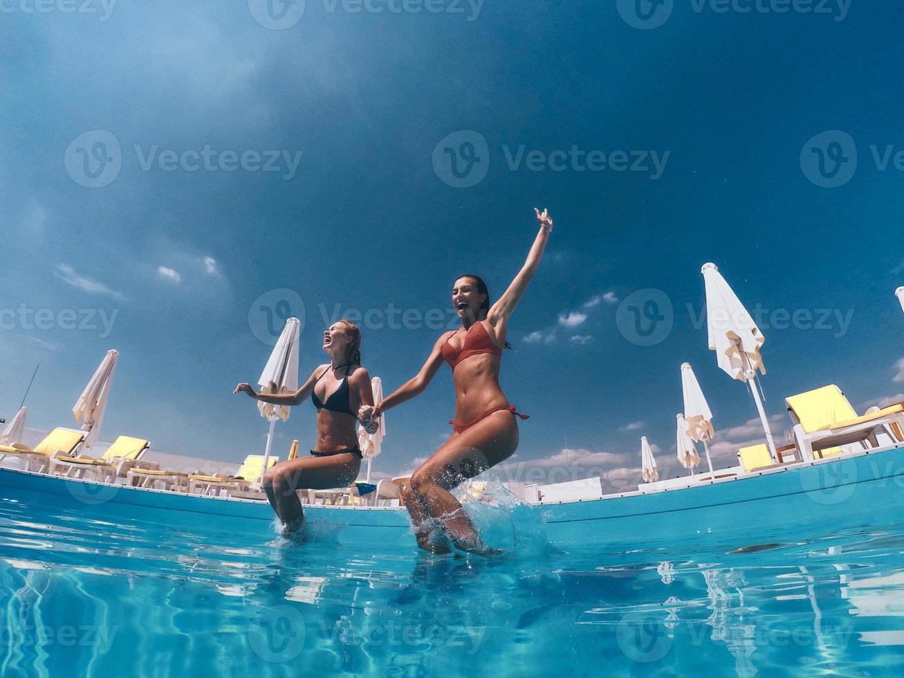 Summer fun. Two attractive young women in bikini jumping in the pool together photo