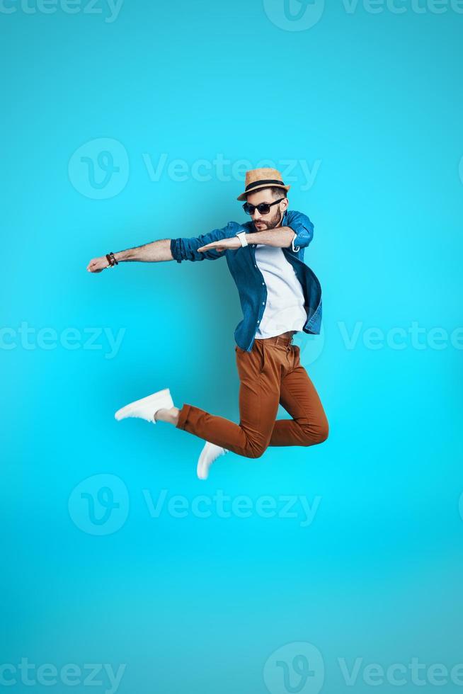 Full length of playful young man dancing while hovering against blue background photo