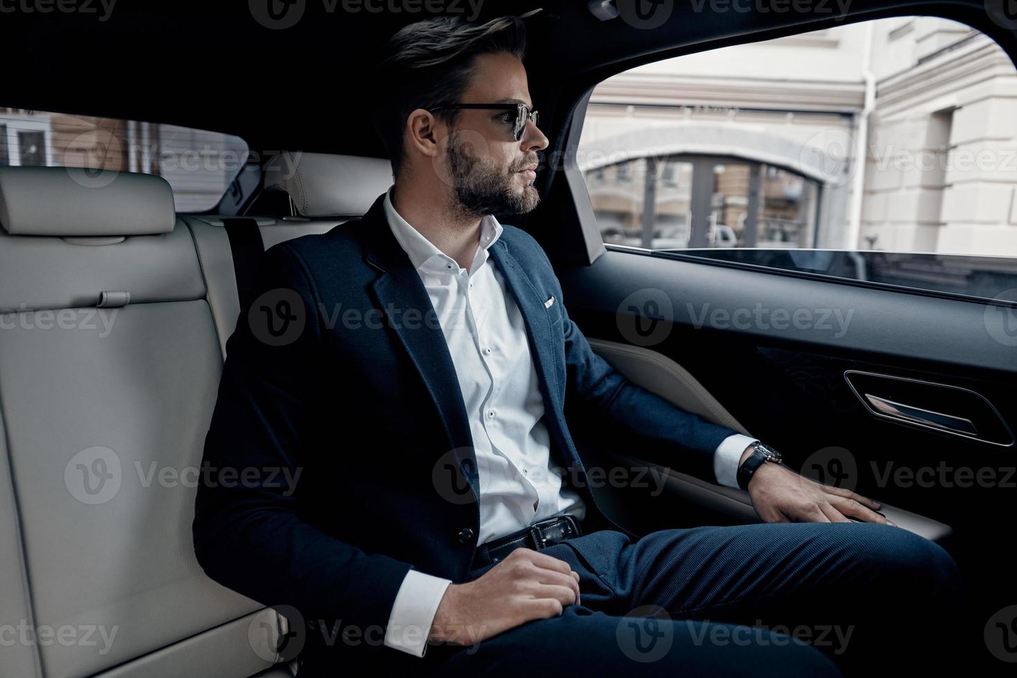 Busy day. Handsome young man in full suit looking through the window while sitting in the car photo