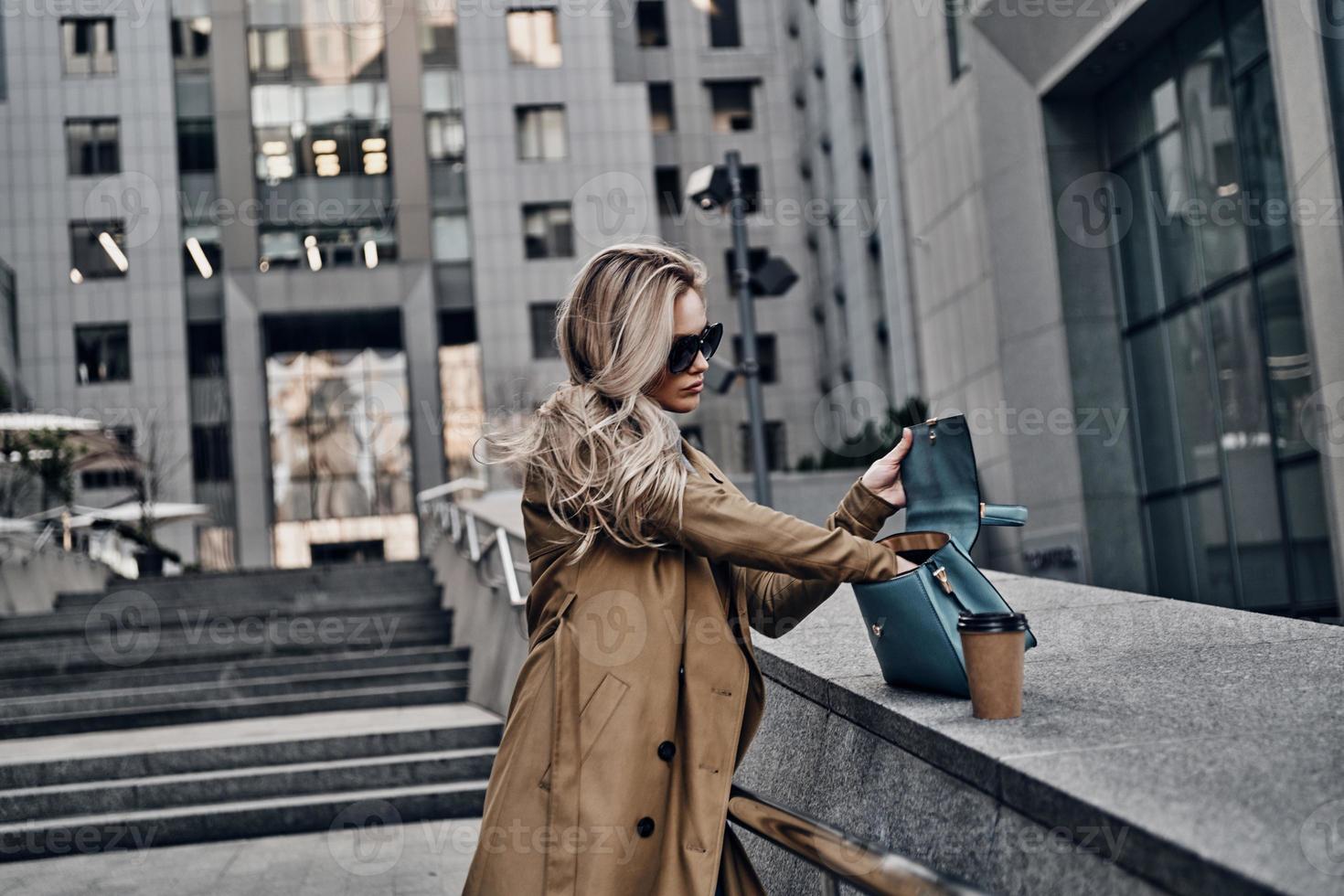 Looking for something. Attractive young woman searching for something in her purse while standing outdoors photo