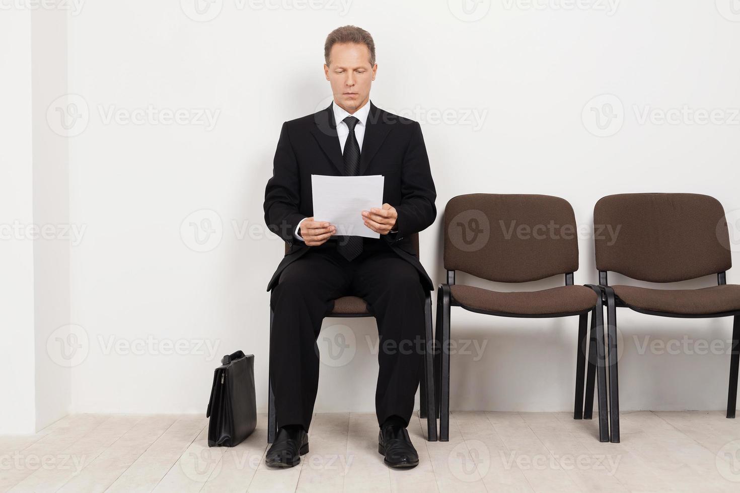 Ready for interview. Thoughtful senior man in formalwear holding paper while sitting at the chair in waiting room photo