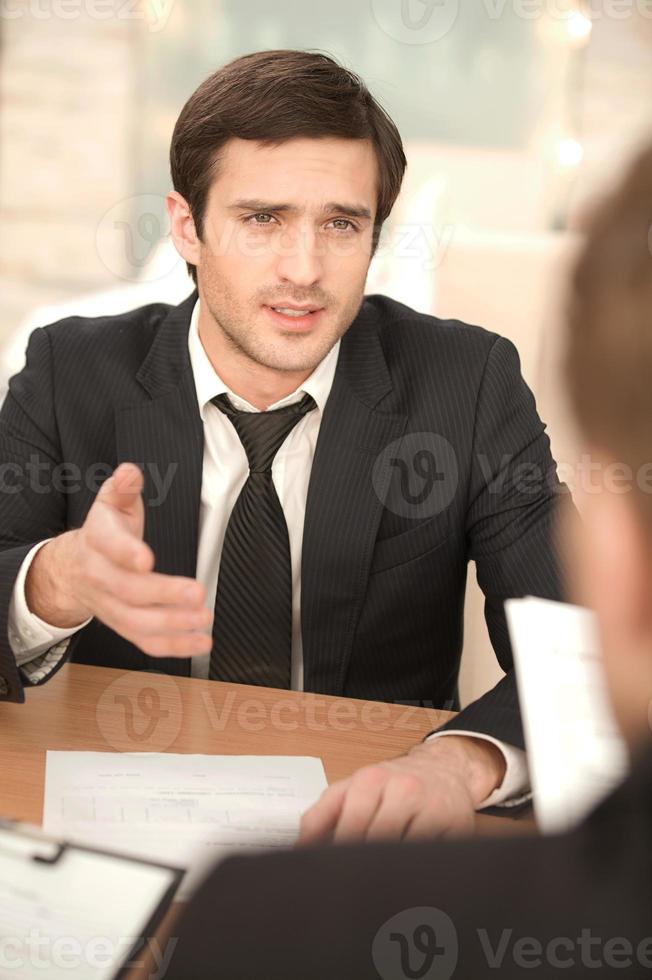 Business conversation. Two business people in formalwear discussing something while sitting at the table photo
