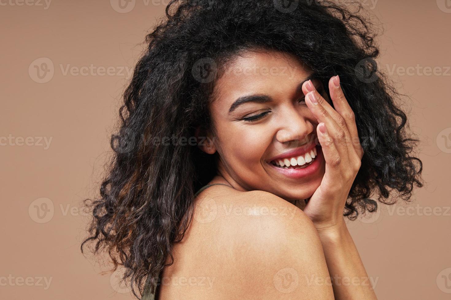 bella joven africana sonriendo y manteniendo los ojos cerrados foto