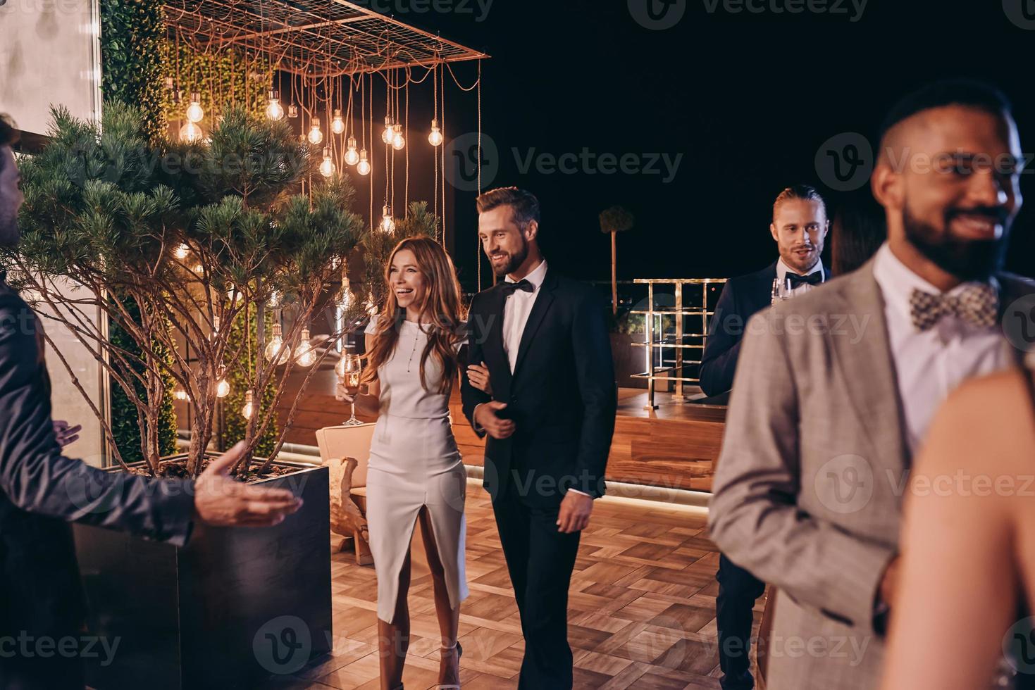 Group of people in formalwear communicating and smiling while spending time on luxury party photo
