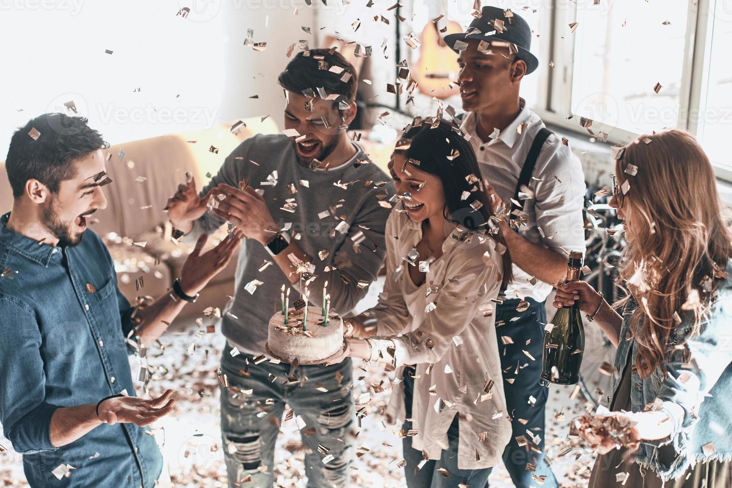 Happy birthday Top view of happy young man celebrating birthday among friends while standing in room with confetti flying around photo