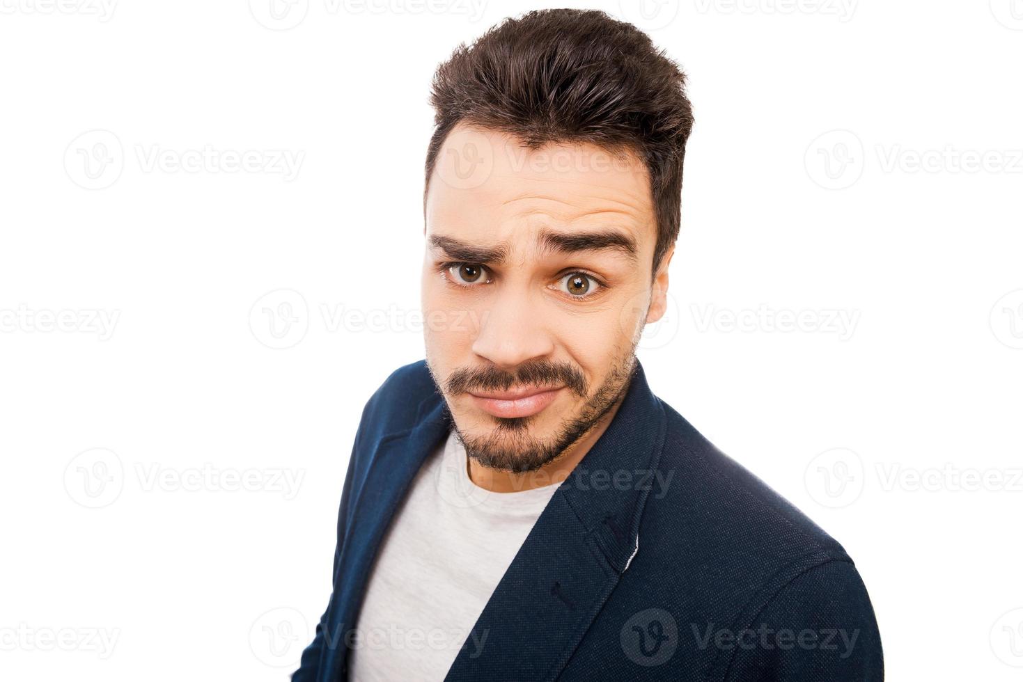 Feeling confused. Confused young man making a face and looking at camera while standing against white background photo