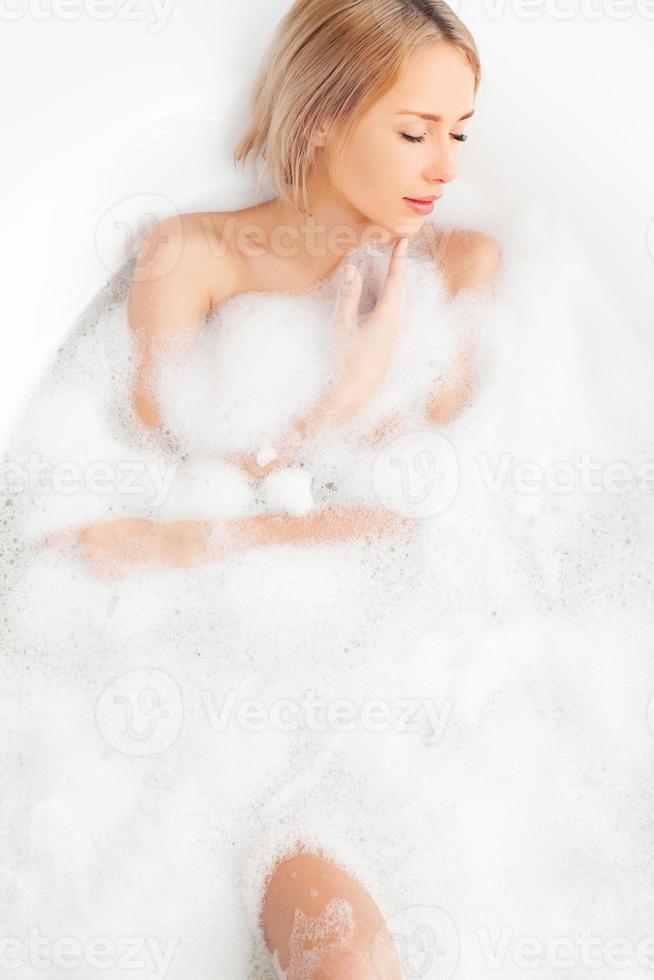 Total relaxation in bath. Top view of beautiful young woman lying in bathtub full of soapy lather and keeping eyes closed photo