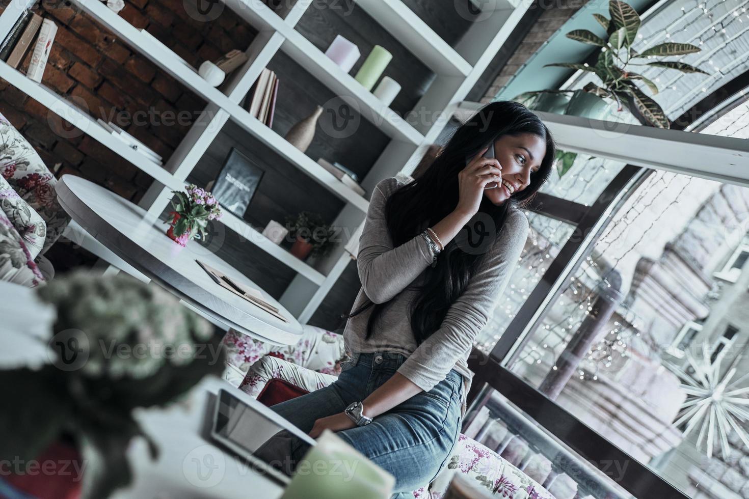 Talking about business. Attractive young smiling woman talking on smart phone and looking over her shoulder while standing in restaurant photo