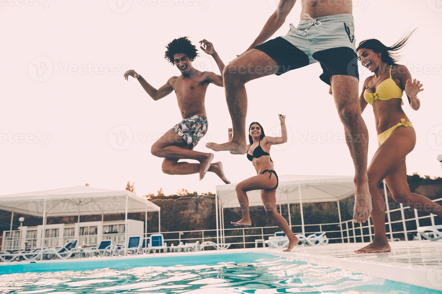 Pool party. Group of beautiful young people looking happy while jumping into the swimming pool together photo