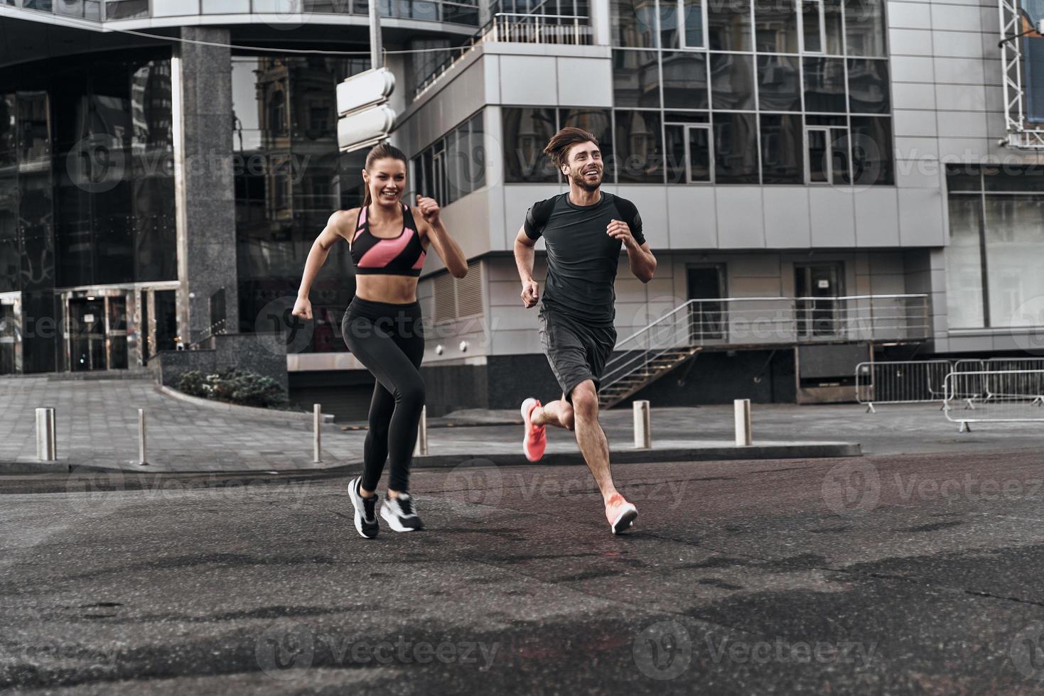 Side by side through the city. Full length of young couple in sport clothing running through the city street together photo