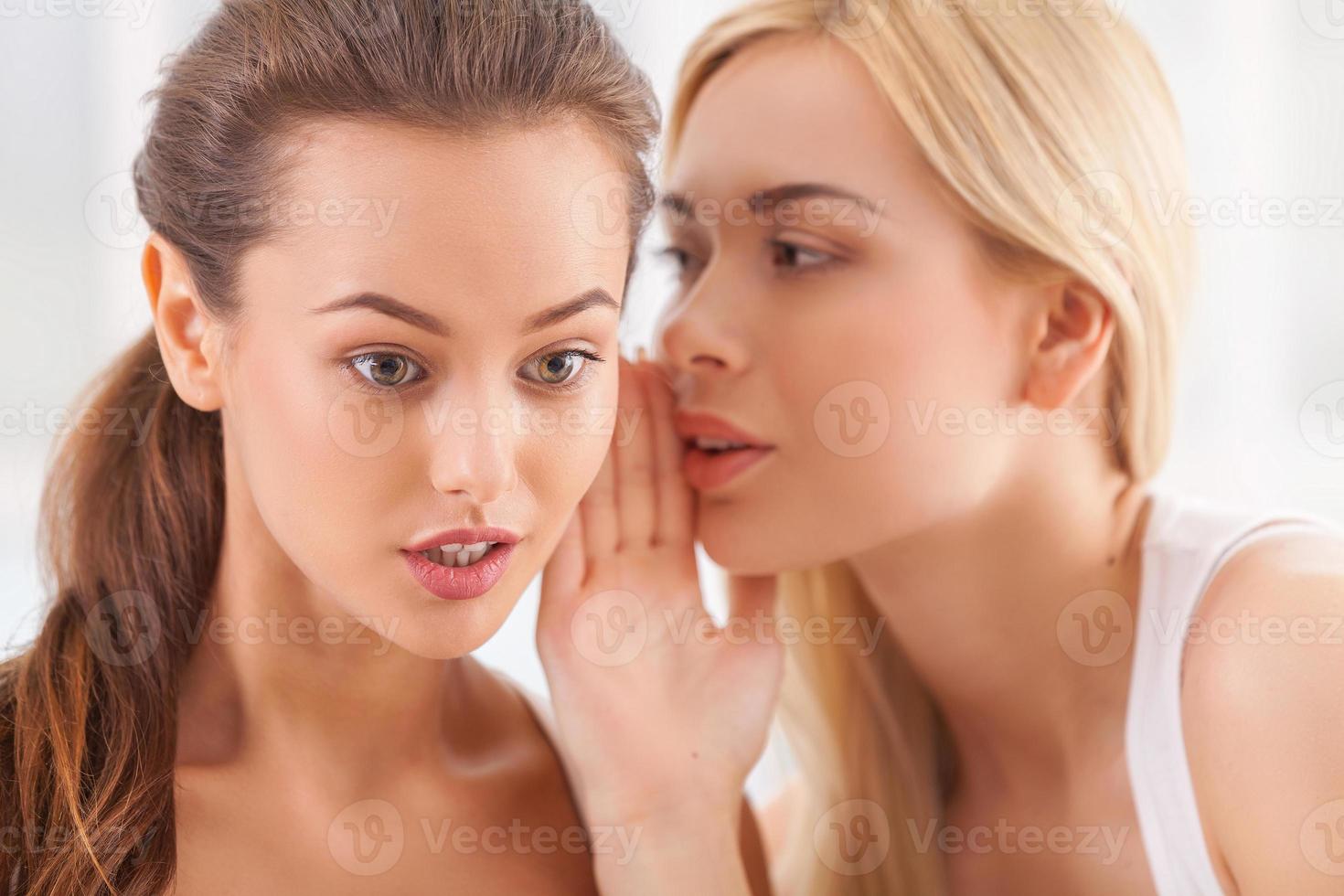 No way news. Beautiful young blond hair woman whispering something to her surprised friend photo