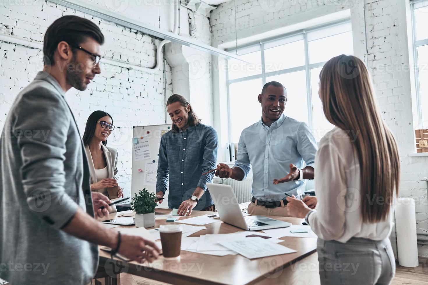 Discussing risky ideas. Group of young modern people in smart casual wear discussing business while standing in the board room photo