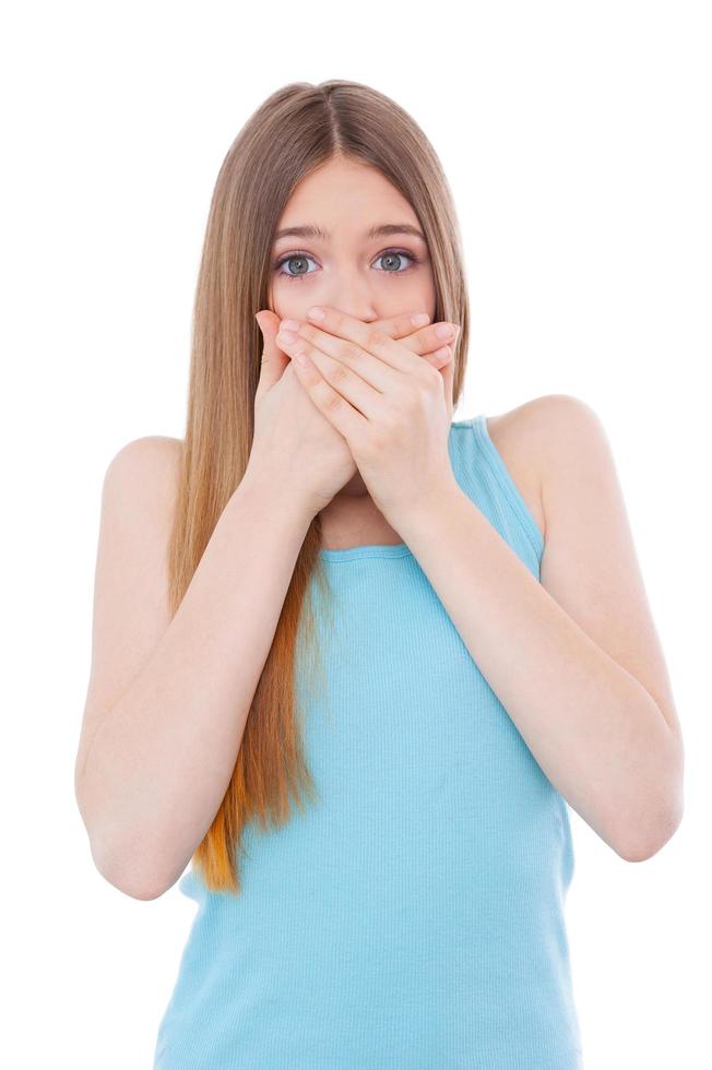 No more gossiping. Shocked young woman covering mouth with hands while standing isolated on white photo