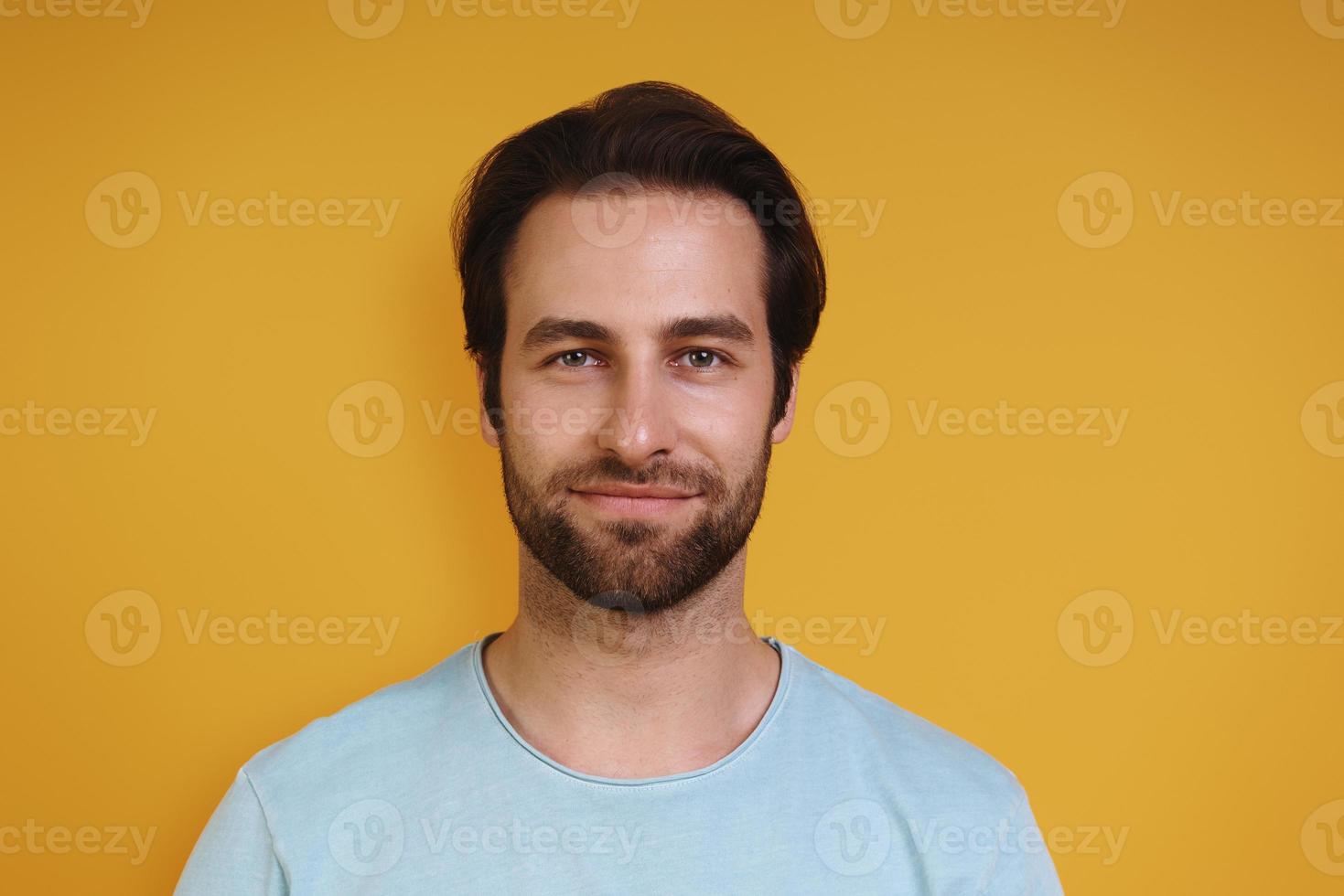 Portrait of young man in casual clothing looking at camera while standing against yellow background photo