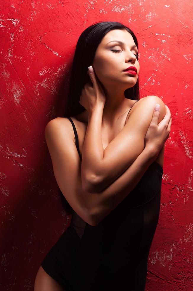 Gorgeous beauty. Beautiful young woman posing and keeping eyes closed while standing against red background photo