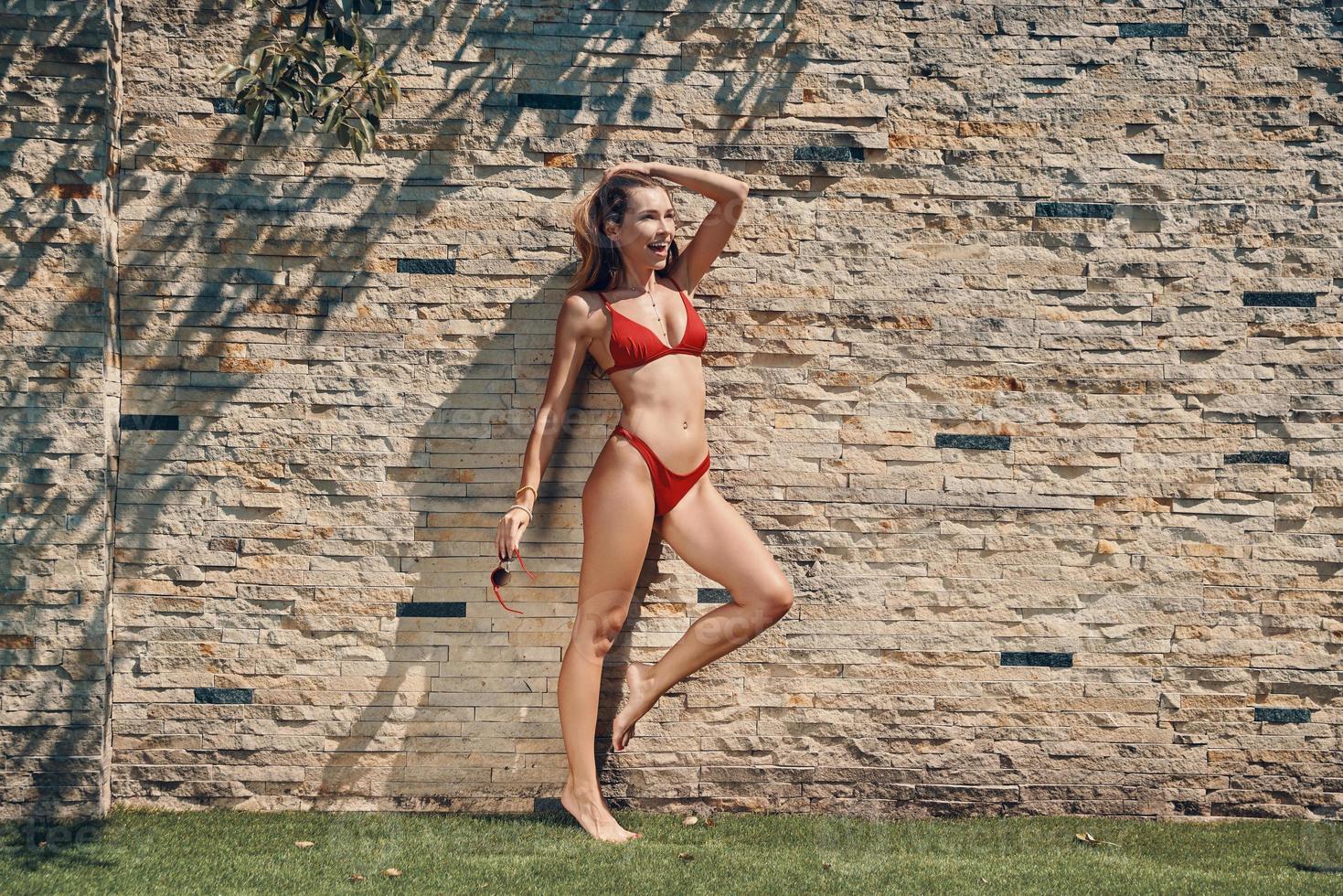 Full length of attractive young woman in bikini looking away and smiling while standing outdoors photo