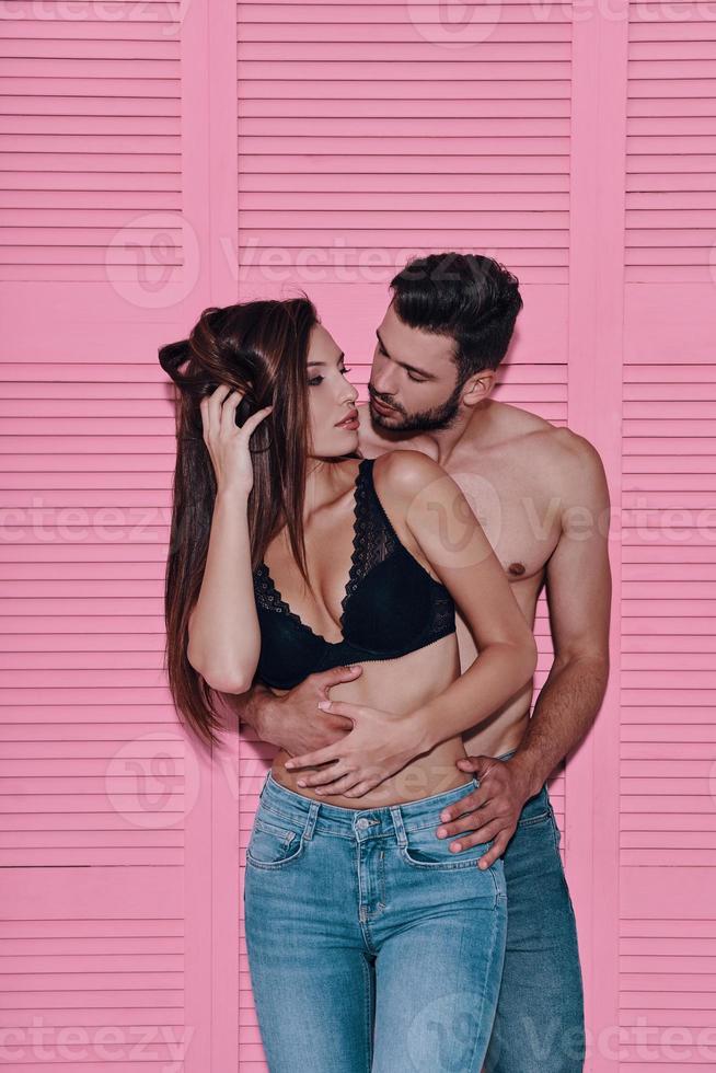 apreciando cada minuto juntos. hermosa joven pareja abrazándose mientras está de pie contra el fondo rosa foto