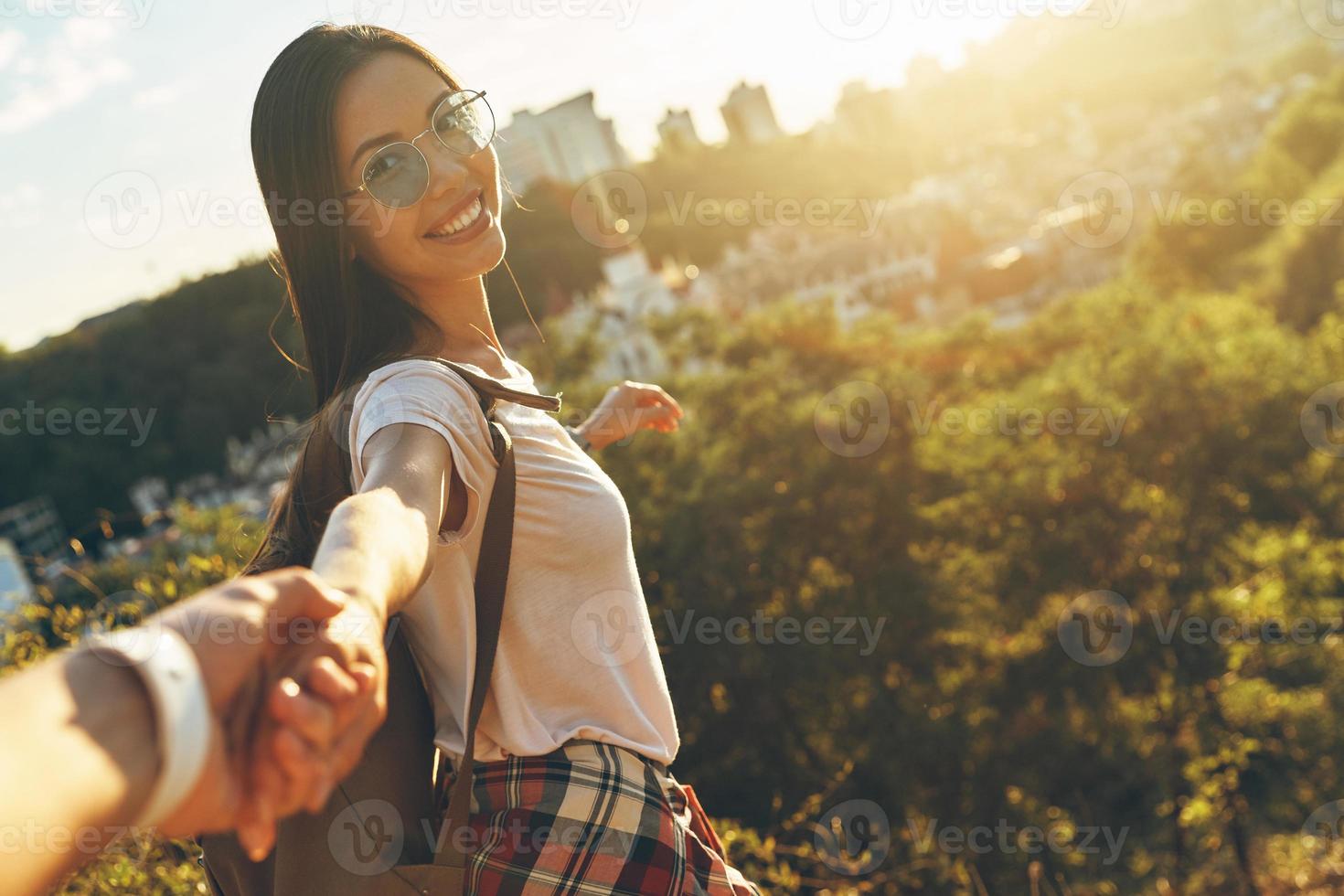 mujer joven feliz mirando a la cámara y sonriendo mientras se toma de la mano con su novio foto