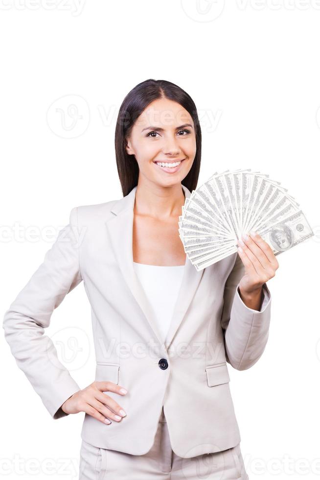 Successful and wealthy. Confident young businesswoman in suit showing money and smiling while standing against white background photo