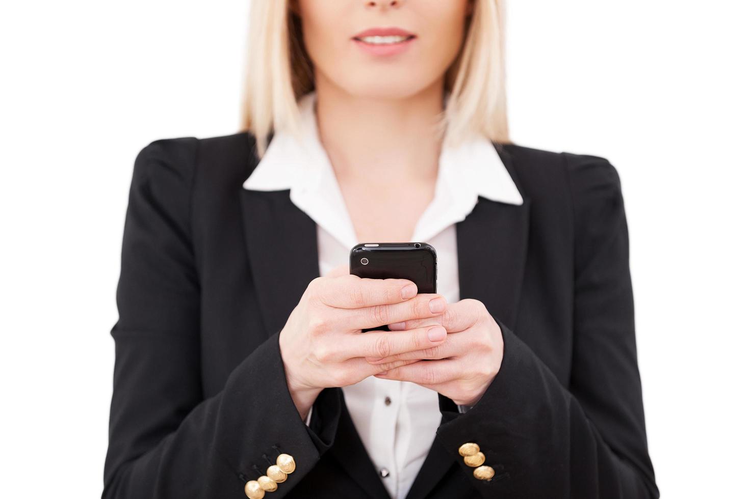 Businesswoman typing a message. Cropped image of mature businesswoman holding mobile phone while standing isolated on white photo