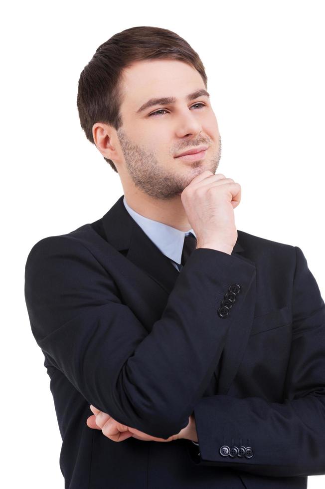 Business dreams. Cheerful young man in formalwear holding hand on chin and looking away while standing isolated on white photo