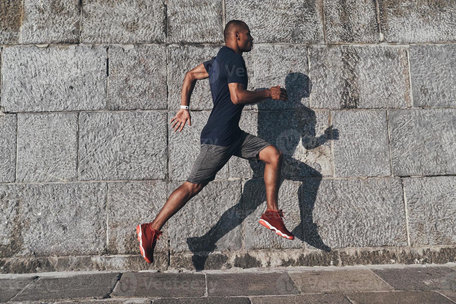 empujando al límite. toda la longitud de un joven africano con ropa deportiva trotando mientras hace ejercicio al aire libre foto