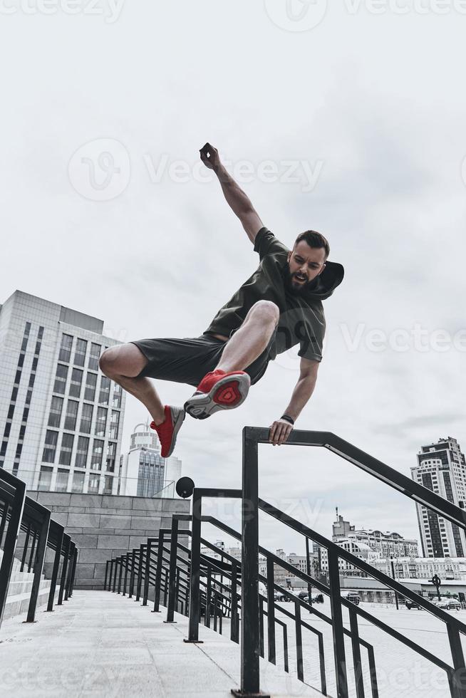 Jumping straight over any obstacles. Full length of handsome young man in sport clothing jumping over railing while exercising outside photo