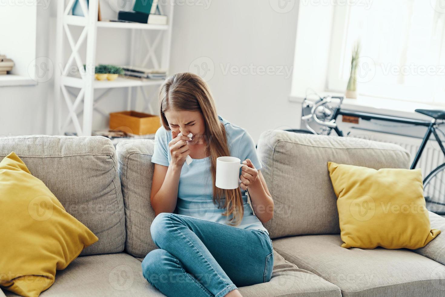 Ill young woman blowing nose and sneezing while sitting on the sofa at home photo