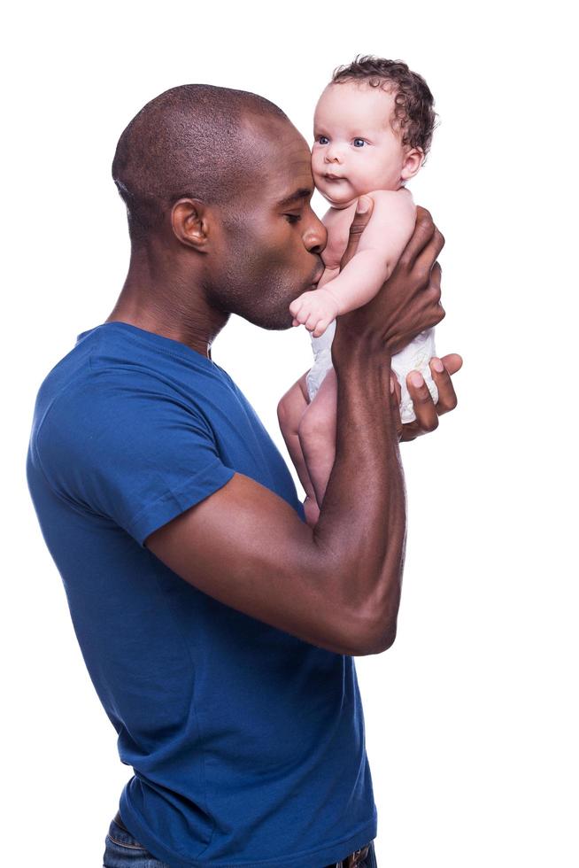 amo a mi bebe. joven africano sosteniendo a su pequeño bebé y besándolo mientras estaba aislado en blanco foto