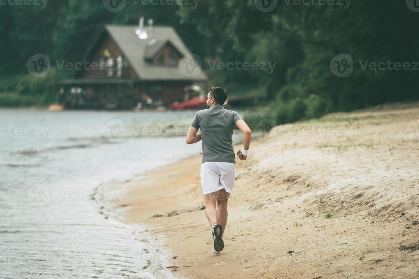 Morning jog. Full length rear view of confident man in sports clothing running along the riverbank photo