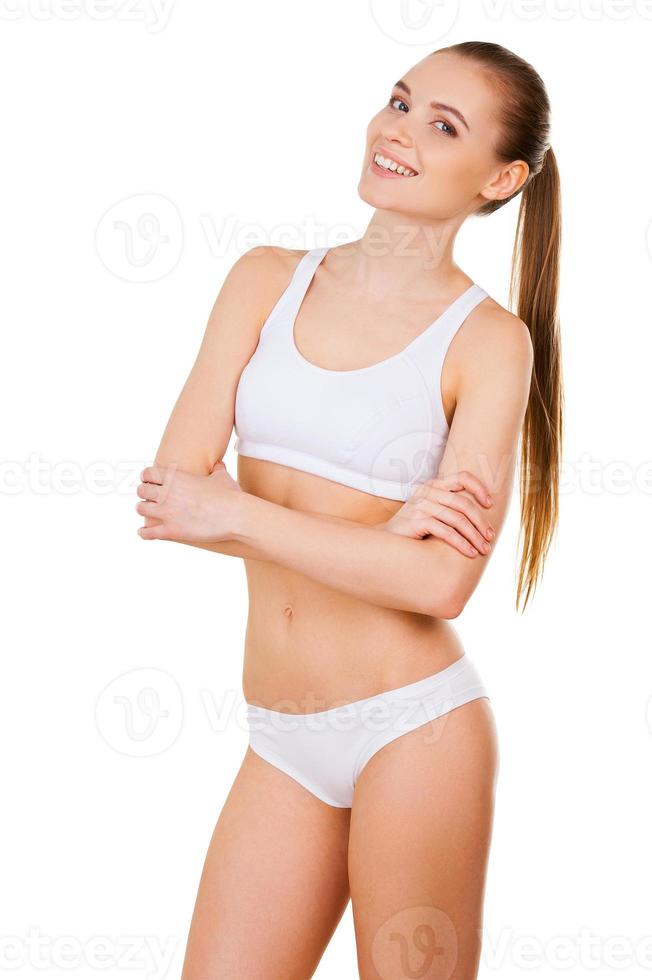 hermosa y saludable. mujer joven atractiva en sujetador blanco y bragas con los brazos cruzados y mirando a la cámara mientras está de pie aislado en blanco foto