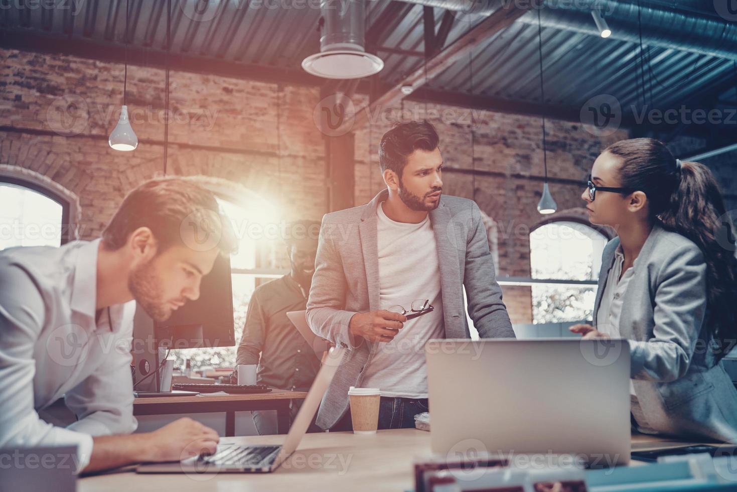 Group of young modern people in smart casual wear communicating and using modern technologies while working in the office photo