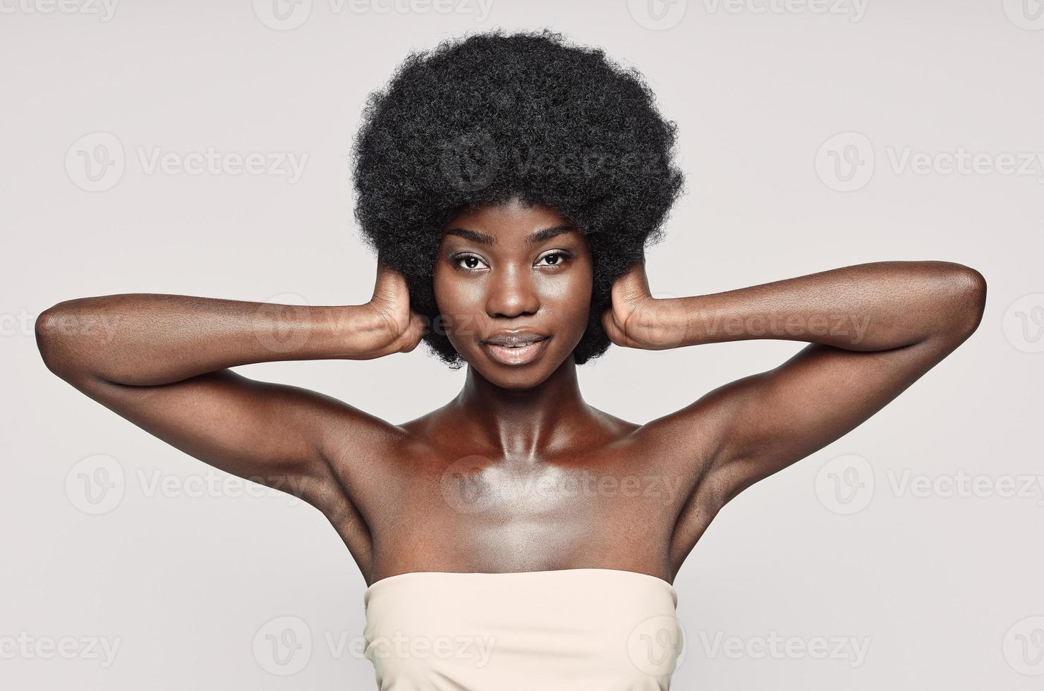 Portrait of beautiful young African woman covering ears with hands while standing against gray background photo