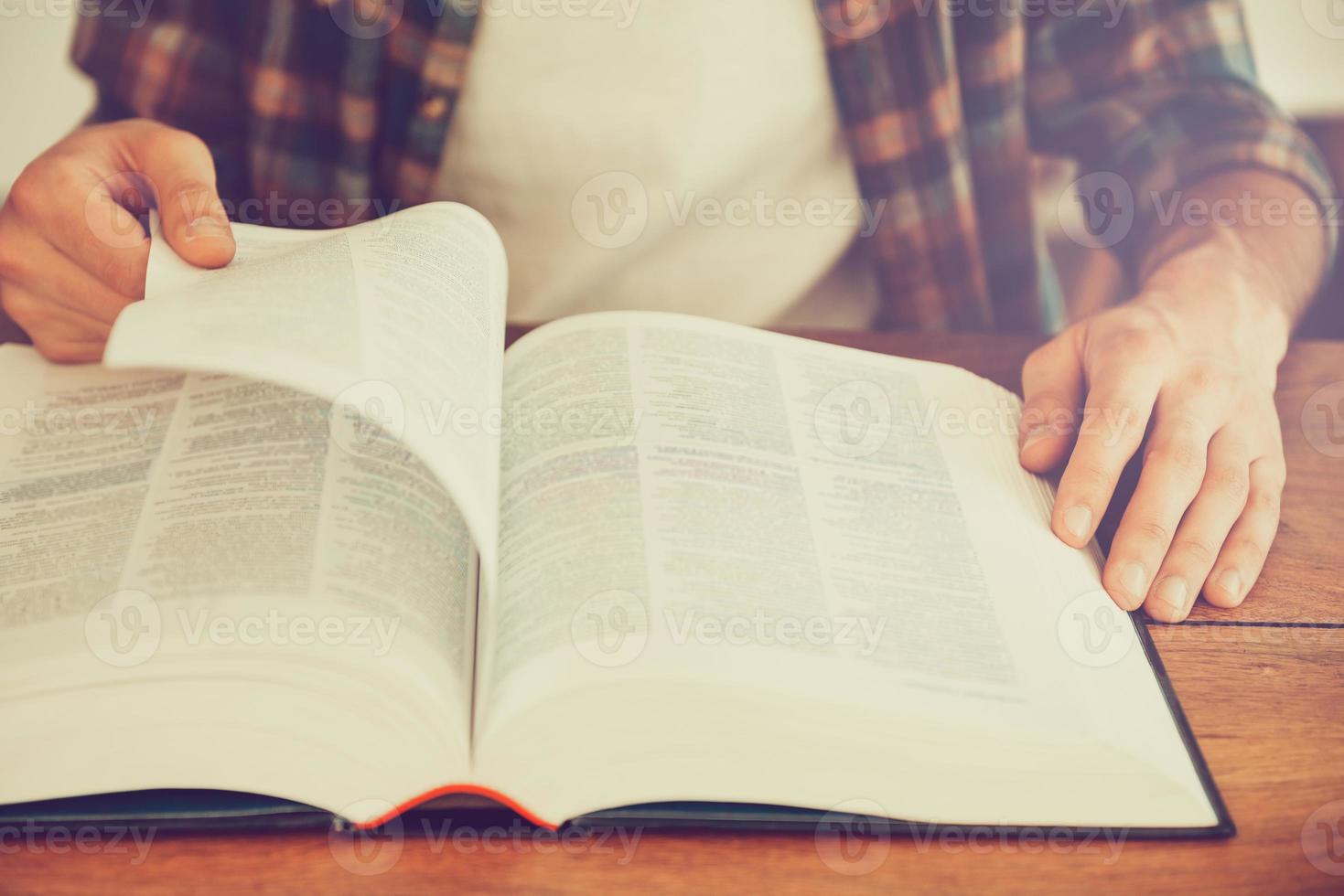 Searching for inspiration in a book. Close-up of man turning the page of book while sitting at the wooden desk photo