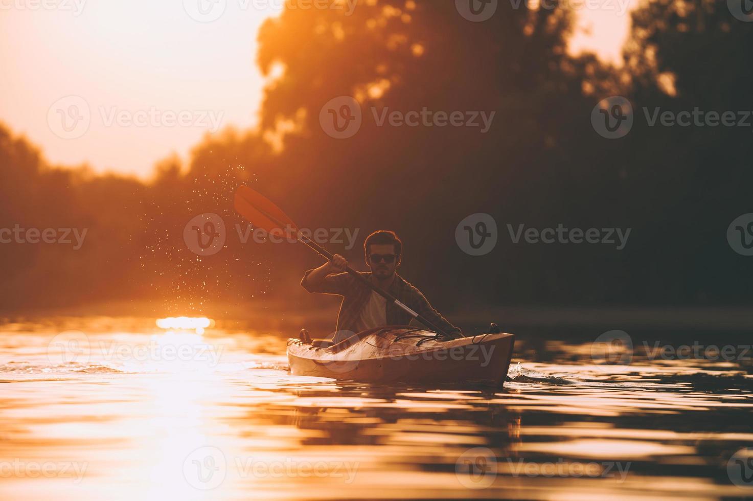 Kayaking is his lifestyle. Young man kayaking on river with sunset in the background photo