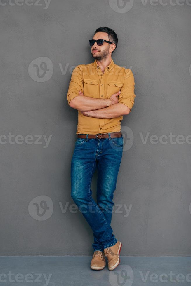 Confident and handsome. Full length of confident mature man in sunglasses keeping arms crossed and looking away while standing against grey background photo