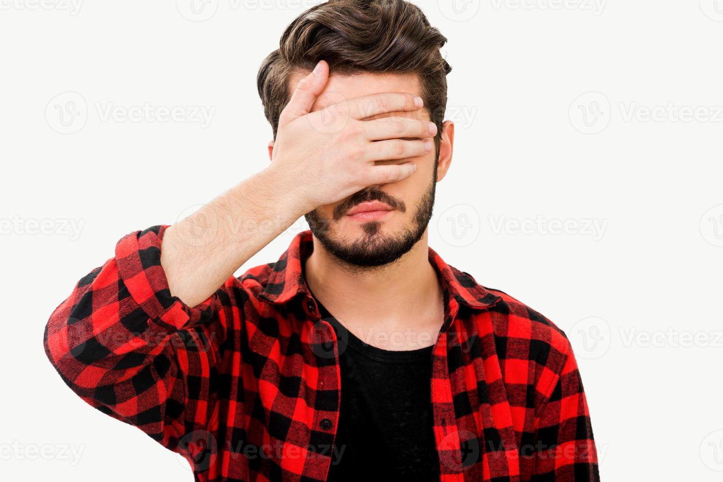 Having some problems. Frustrated young man covering his face by hand while standing against white background photo