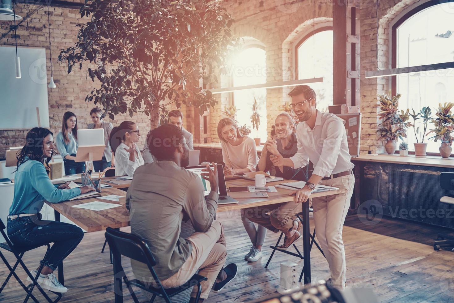 Group of young modern people in smart casual wear communicating and using modern technologies while working in the office photo
