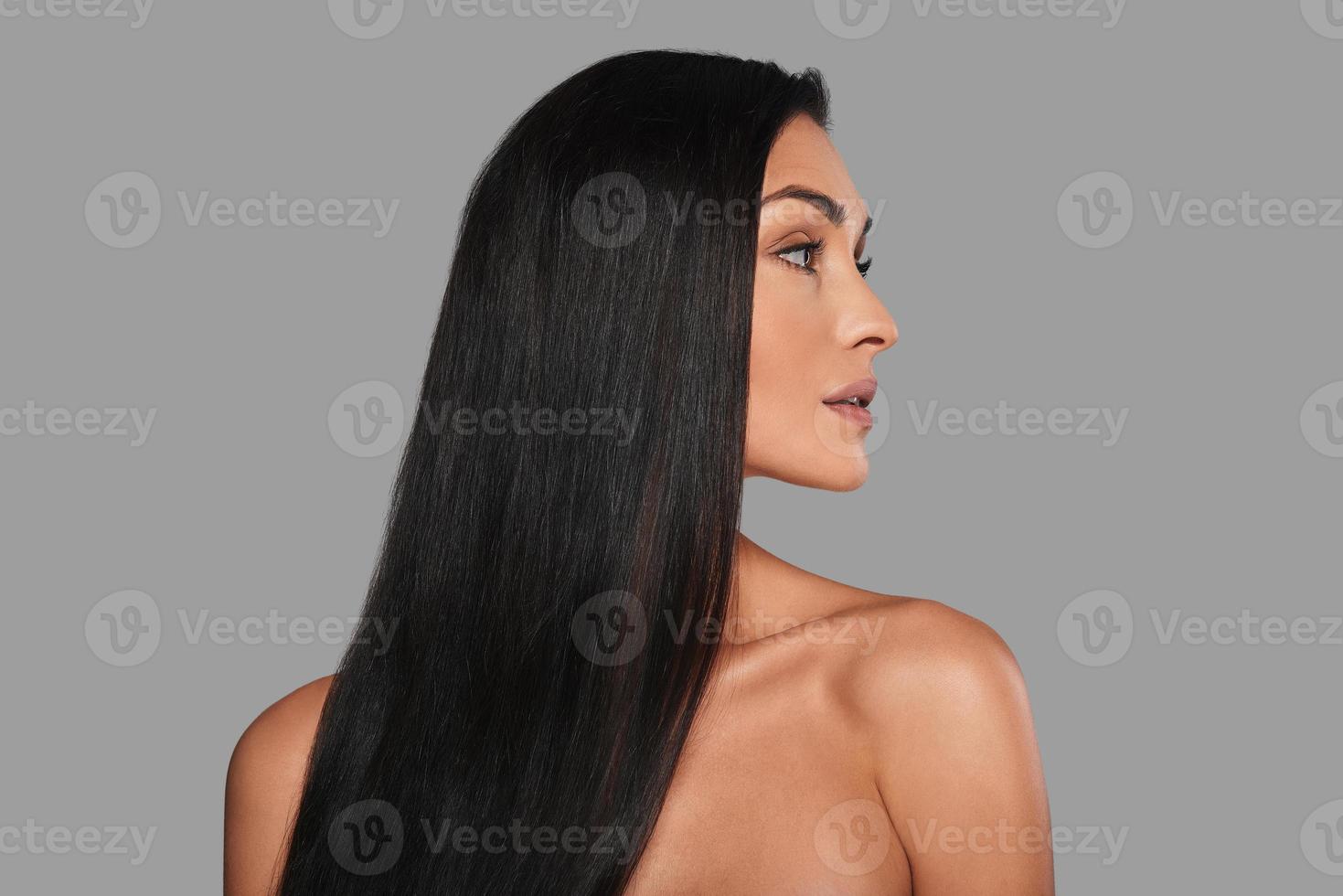 Perfect hair. Attractive young woman looking away while standing against grey background photo