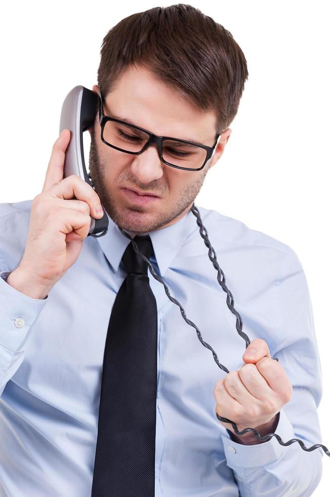 Fed up of office life. Furious young man in shirt and tie talking on telephone and expressing negativity while standing isolated on white photo