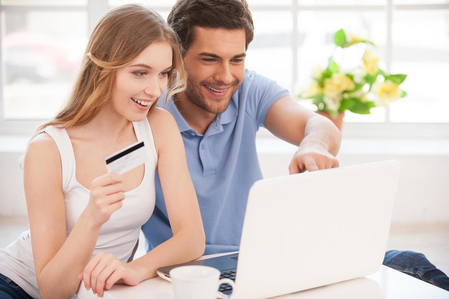 Las compras por Internet son divertidas. alegre pareja joven comprando en la red mientras se sientan cerca uno del otro y miran la computadora portátil foto