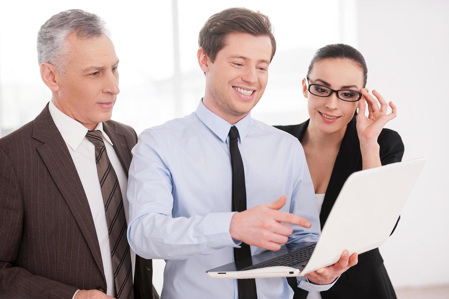 Working on project together. Three confident business people discussing something while looking at the laptop photo