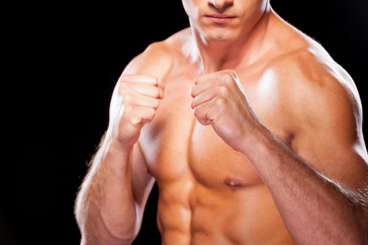 Ready to fight. Close-up of serious young shirtless man looking at camera while standing against black background photo