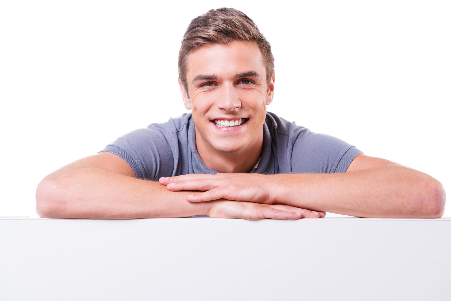 Confident handsome. Handsome young man looking at camera and smiling while keeping arms crossed and leaning at the copy space photo