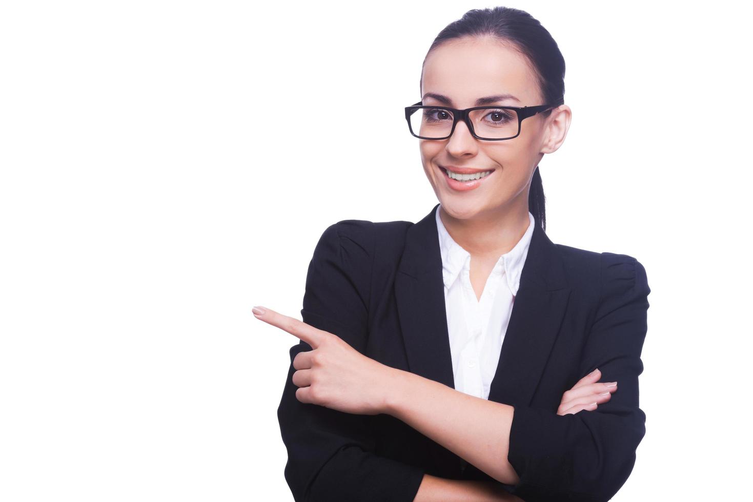 mujer de negocios señalando el espacio de la copia. hermosa mujer joven en ropa formal y anteojos apuntando hacia afuera y sonriendo mientras está de pie aislado en blanco foto