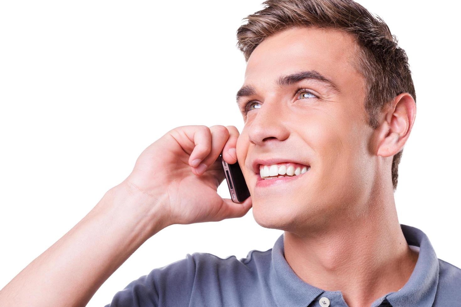 buena plática. joven feliz hablando por teléfono móvil y sonriendo mientras está de pie aislado en fondo blanco foto