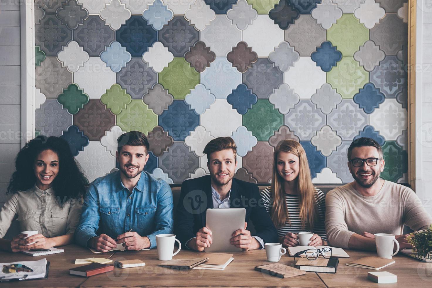 Dream team. Cheerful young people looking at camera with smile while sitting at the office table on business meeting photo