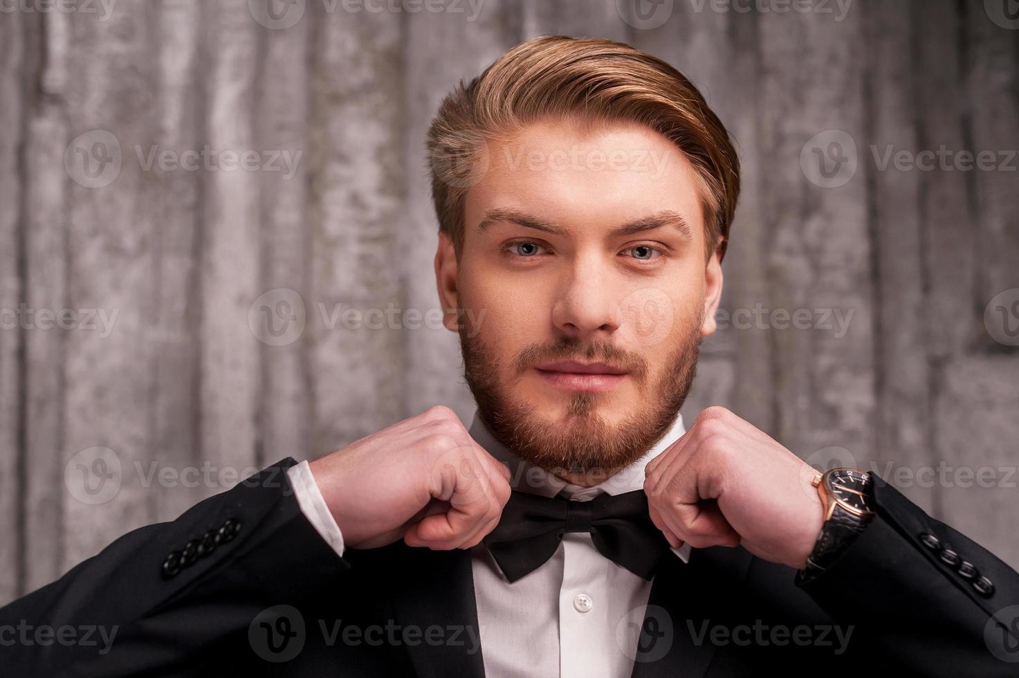 Tying a bow tie. Handsome young man in formalwear adjusting his bow tie and looking at camera photo