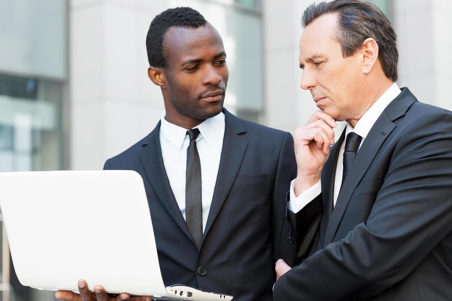 pidiendo un consejo experto. dos hombres de negocios confiados que miran la computadora portátil mientras uno de ellos sostiene la mano en la barbilla foto